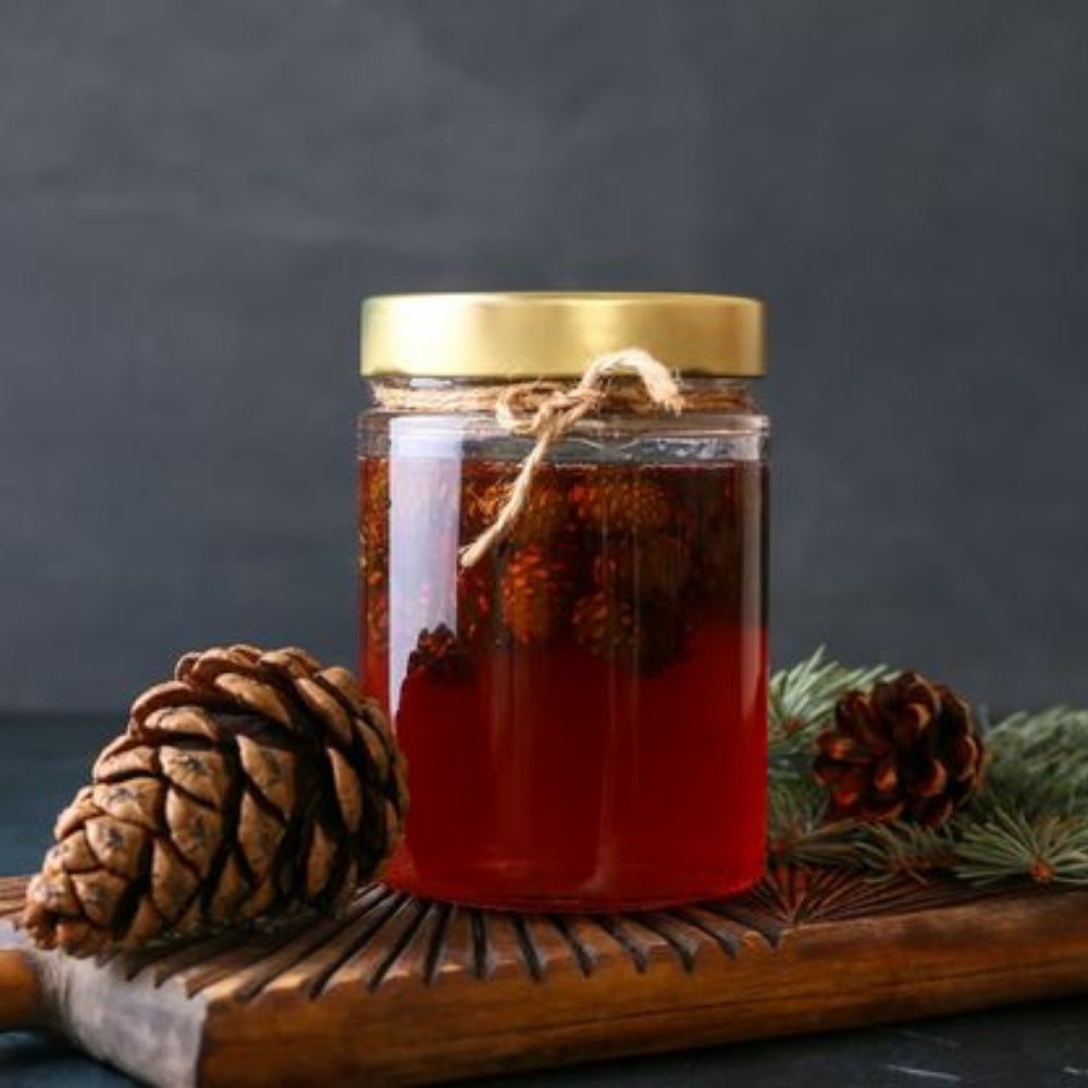 Zonnige pot Dennenappelstroop van Mijn winkel, omringd door dennenappels en takken, perfect voor het toevoegen van natuurlijke zoetheid aan gerechten.