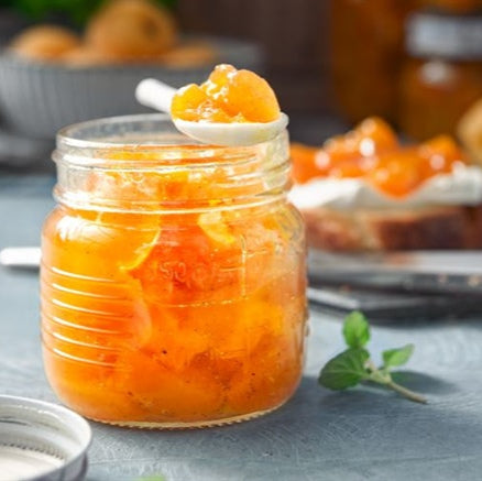 Een pot Abrikozen Jam van 750G van Mijn winkel, met een gouden kleur en een lepel vol jam. Perfect voor desserts of gewoon om zo van te genieten.