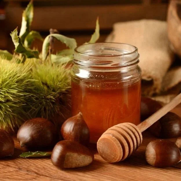 Kastanje honing van Mijn winkel in een glazen pot, omringd door kastanjes en bladeren. De ambachtelijke honing heeft een krachtige smaak en is perfect voor liefhebbers van karaktervolle honing.