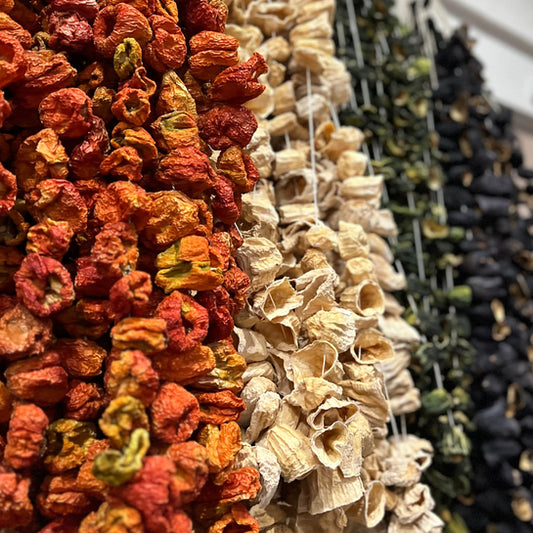 Een kleurrijke rij gedroogde paprika's van Mijn winkel, met een mix van rode, groene en zwarte variëteiten, perfect voor het toevoegen van rijke, intense smaak aan gerechten. Gedroogde Paprika voor een volle, rokerige smaak met een vleugje zoetheid.