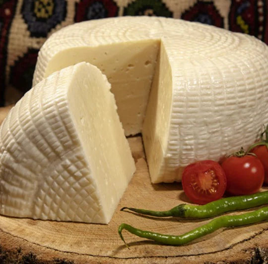 Vers gesneden Mandenkaas (Sepet Peyniri) van Mijn winkel, een authentieke Turkse kaas met een unieke structuur en romige smaak, geserveerd met tomaat en groene peper op een houten plank.