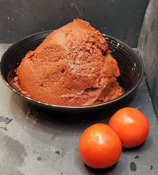 Biologische tomatenpasta uit Antep in een zwarte kom met verse tomaten van Mijn winkel.