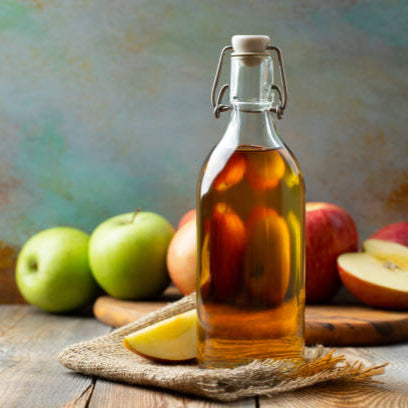 Fles biologische appelazijn van Mijn winkel, omringd door verse appels op een houten tafel. Perfect voor een gezonde levensstijl.